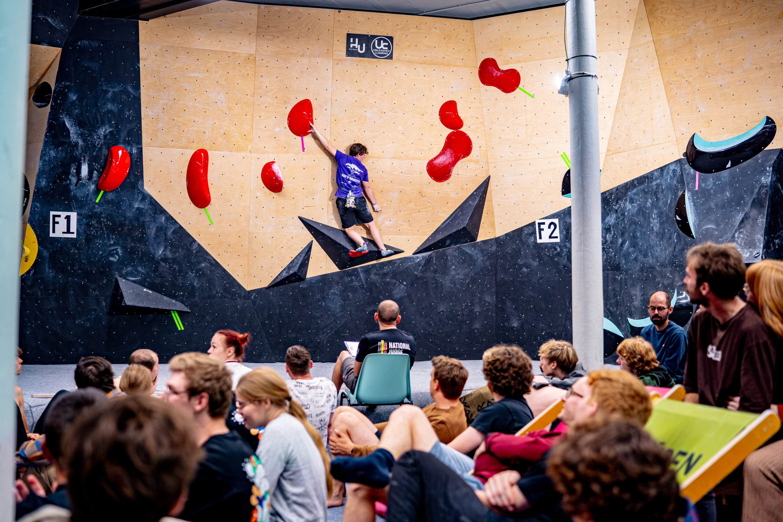 Competitie events bouldering Walden gent: Klimmer in actie tijdens de finales van een bouldering competitie bij Walden Gent, met publiek dat de prestaties volgt.